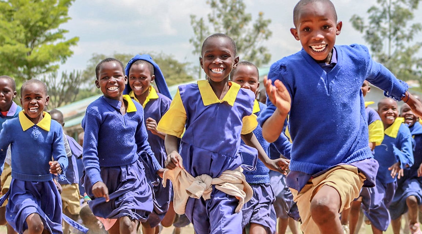 Primary school children in blue uniforms running towards the camera, laughing